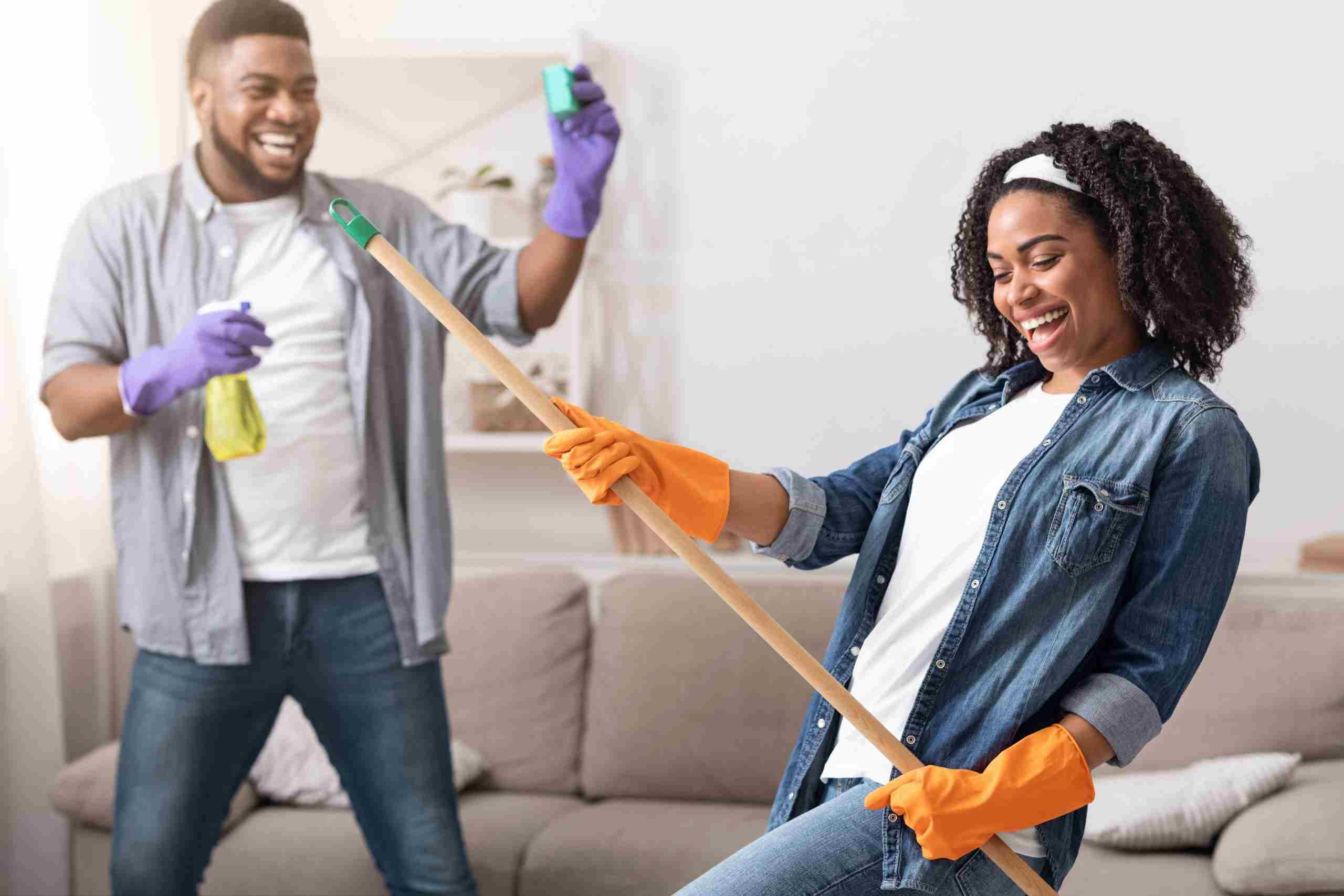 Man and woman with cleaning gloves, playfully enjoying cleaning their living room