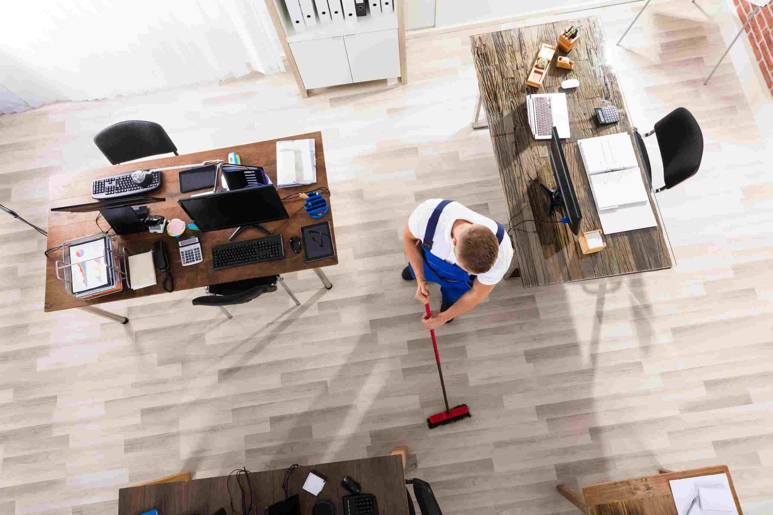 Man in blue jumpsuit keeping collaborative workspace clean with a broom