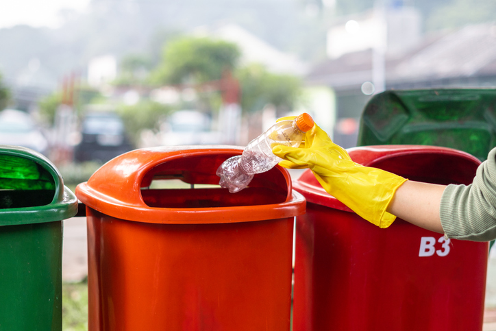 A person throwing the empty bottle into the proper bin to avoid recycling mistakes.