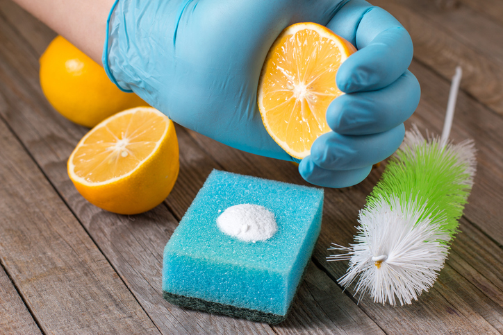 A man is squeezing a lemon with baking soda on a sponge to promote green cleaning using eco-friendly ingredients.