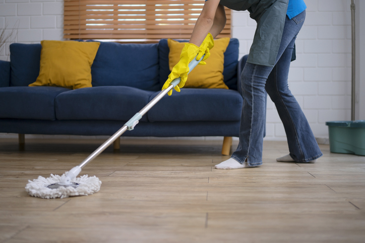 A woman is mopping the hardwood floor to remove salt stains as part of the winter cleaning tips for Calgary homes.